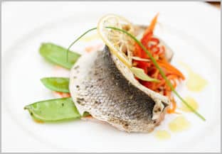 A large white plate with carefully arranged grilled seabass